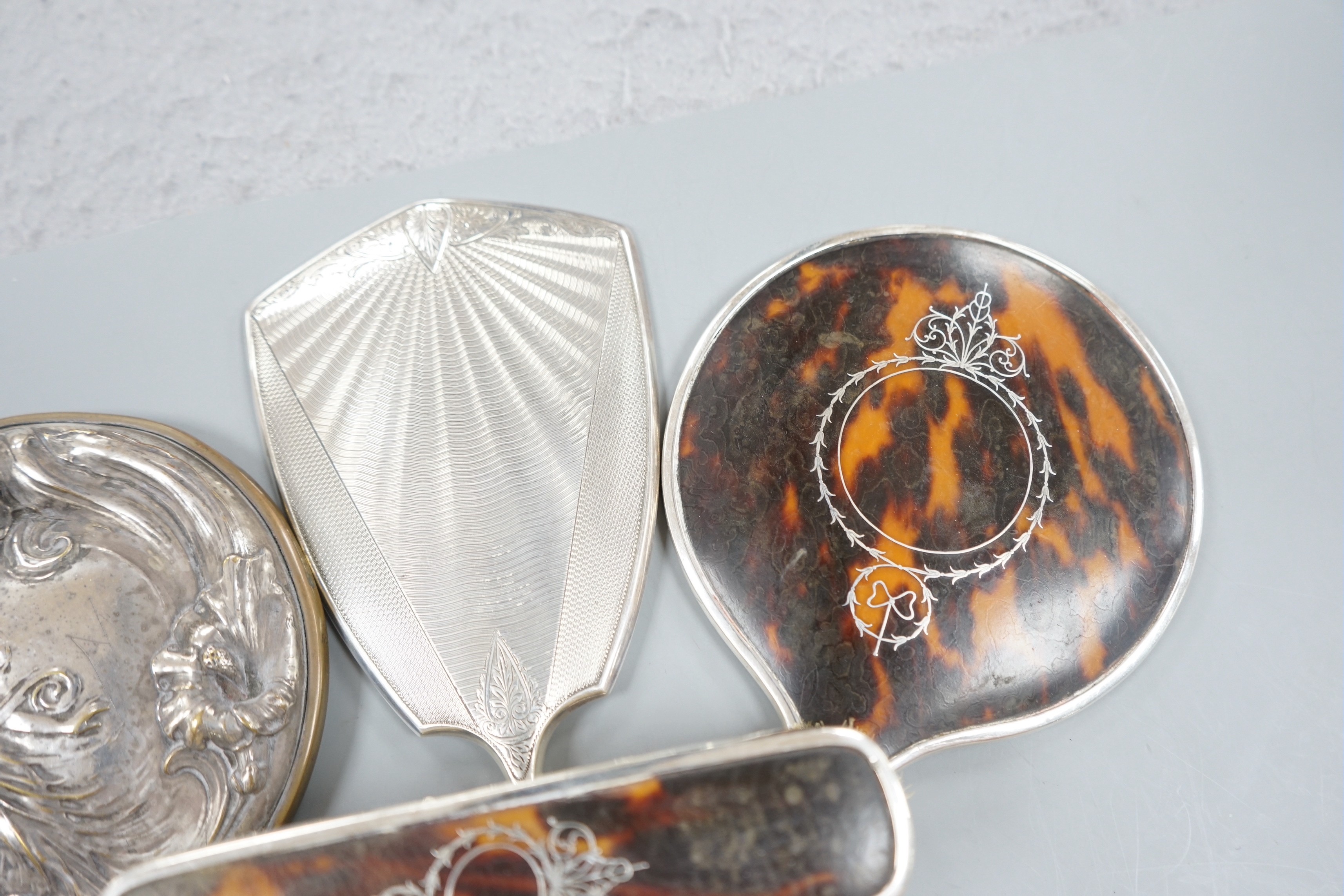 A George V silver and tortoiseshell mounted hand mirror and clothes brush, one other silver mounted hand mirror and a plated hand mirror.